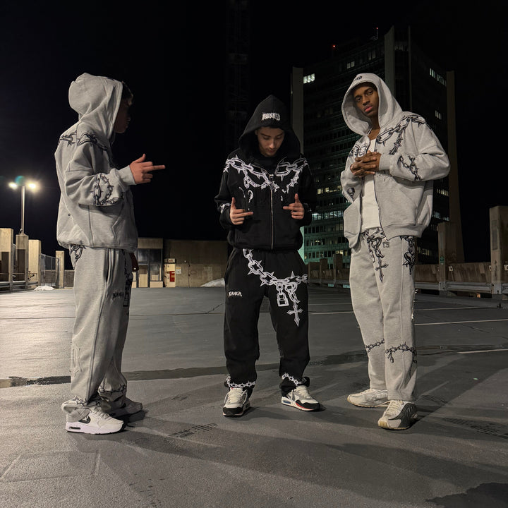 Two people in matching outfits standing on a street at night.