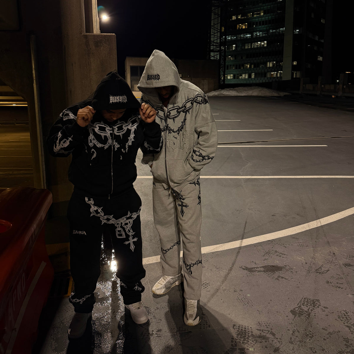 Two people in matching outfits standing on a rooftop at night with city lights in the background.