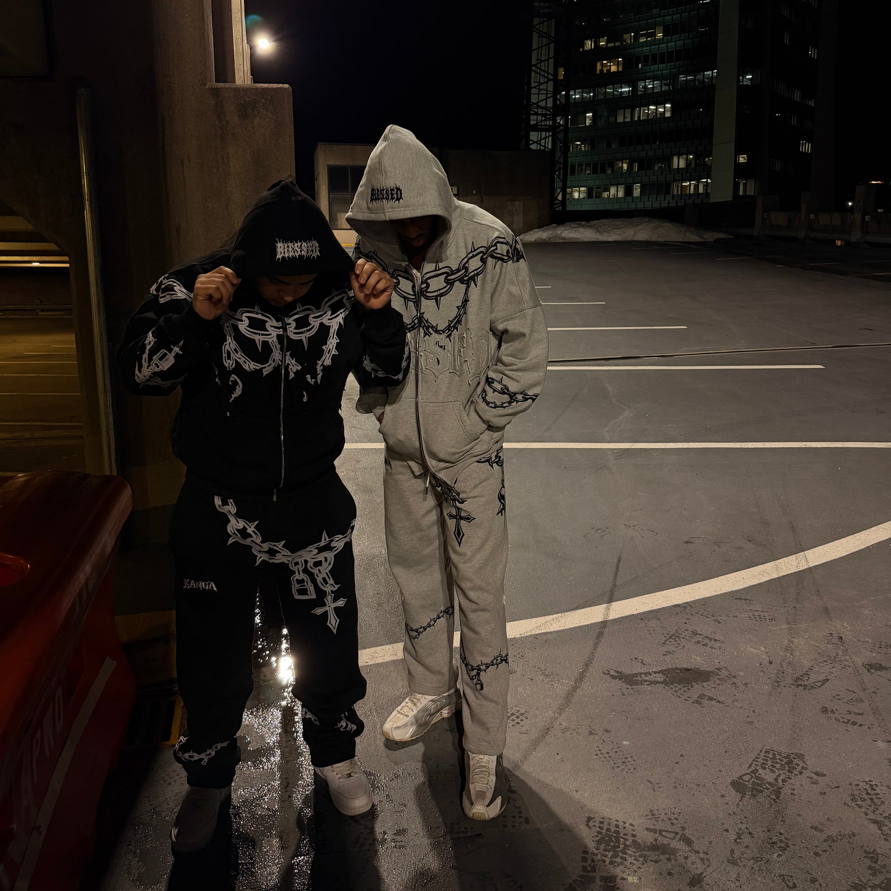 Two people in matching outfits standing on a rooftop at night with city lights in the background.