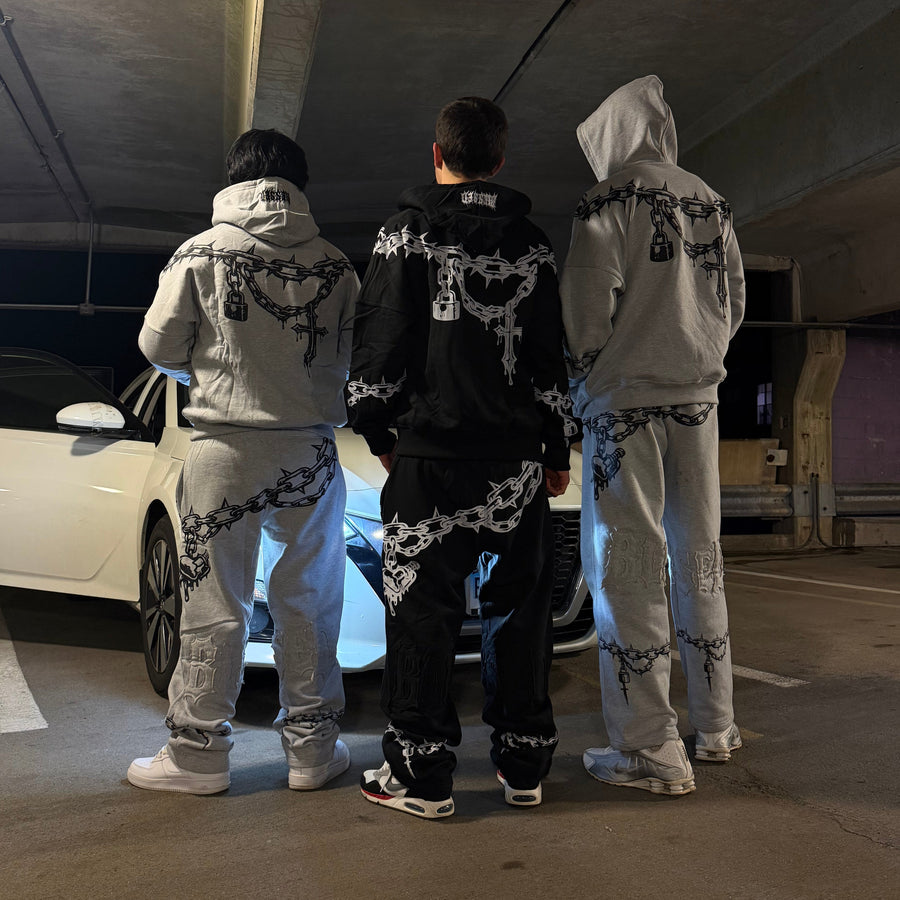 Three people wearing matching outfits with chains in a room.
