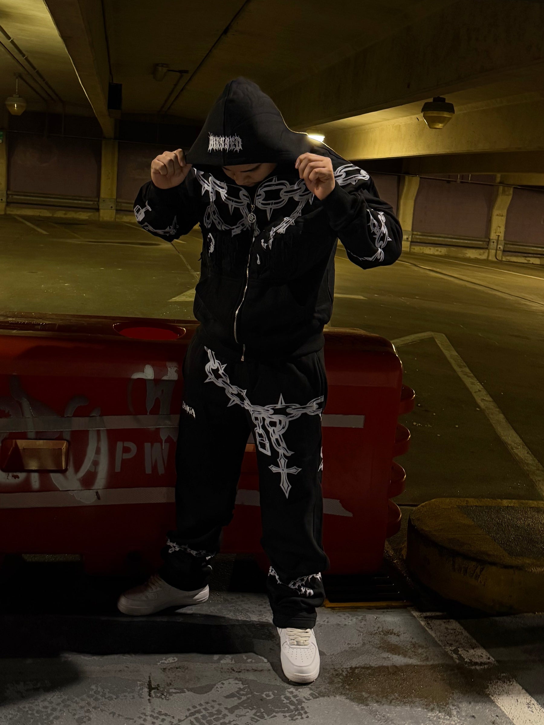 Person in a dark outfit with white patterns standing in a dimly lit room.