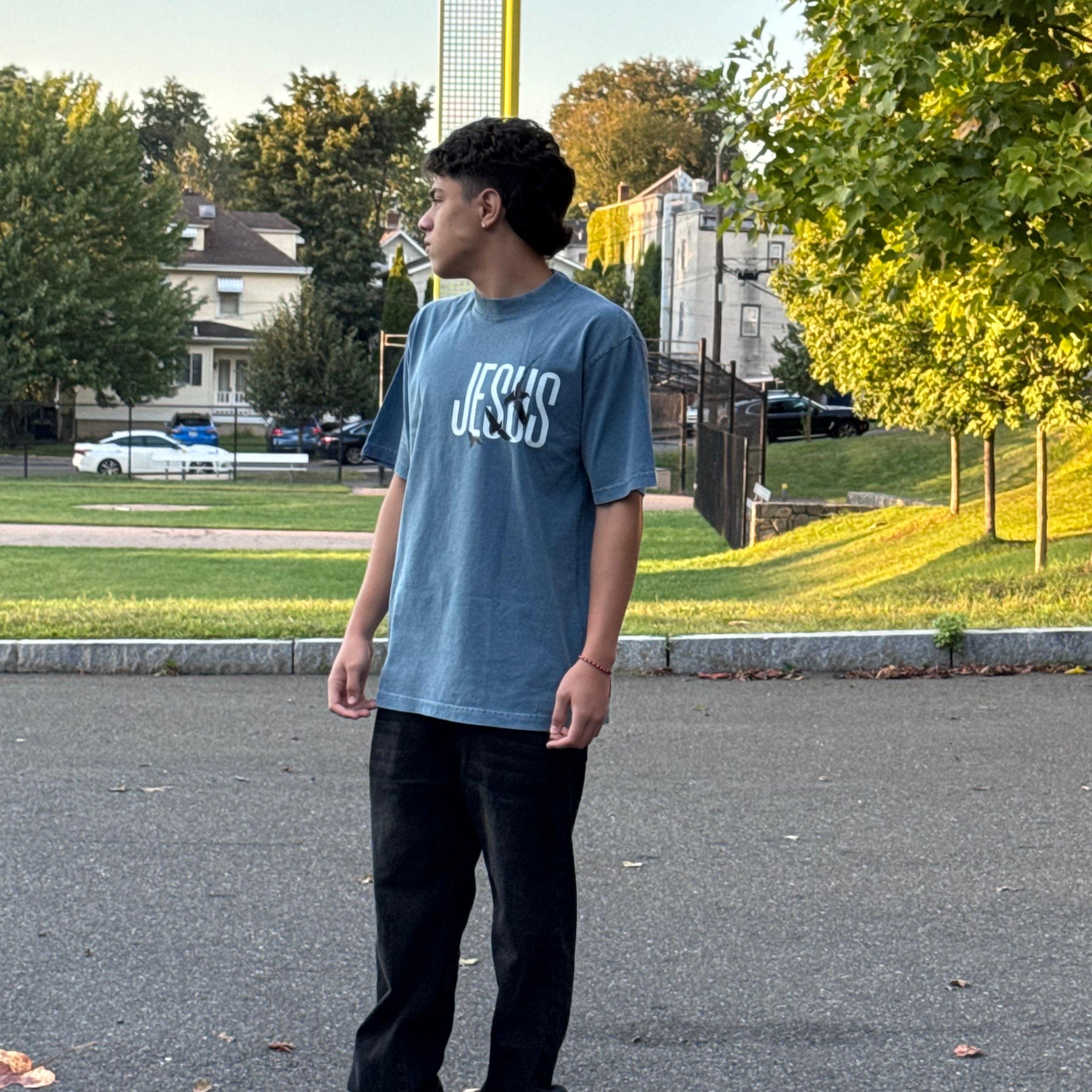 Person wearing a blue t-shirt with text, standing on a street with trees and houses in the background.
