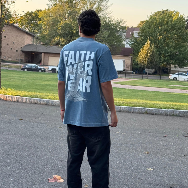 Person wearing a blue t-shirt with 'FAITH OVER FEAR' text, standing on a street.